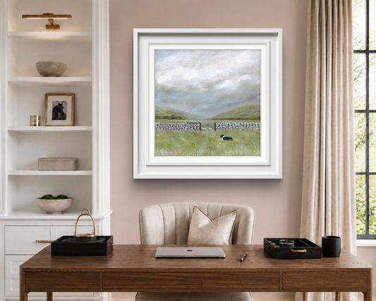 Home office with a wooden desk and shelves, with a  framed landscape painting featuring a wide sweeping countryside with a sheepdog and dry stone wall