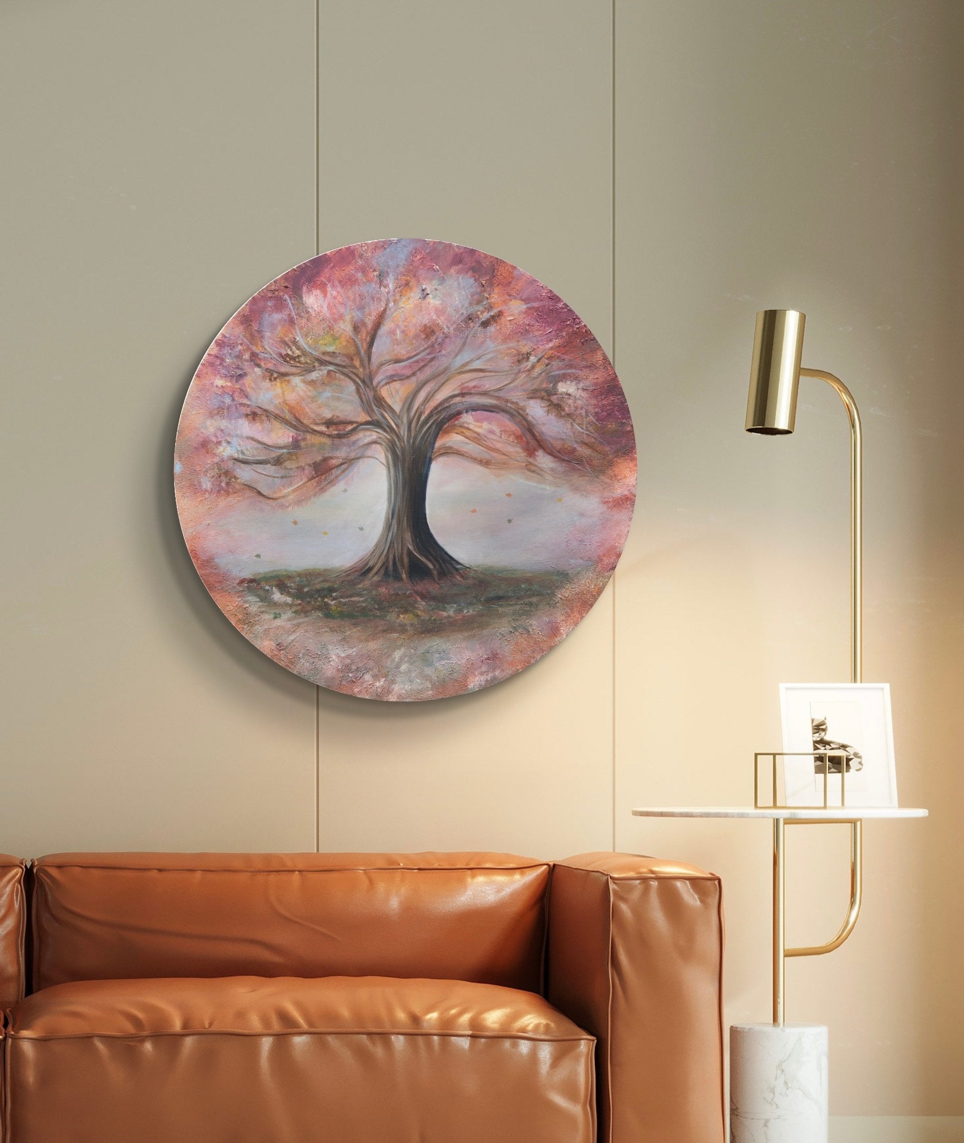 An original acrylic painting of a tree with autumn leaves, mounted on a wall above a leather sofa, with a lamp and a small wooden stool beside it.