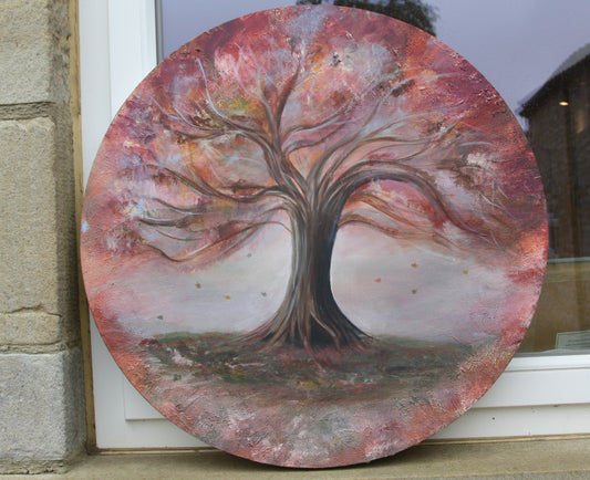 A circular canvas on a windowsill depicting an autumn tree painting