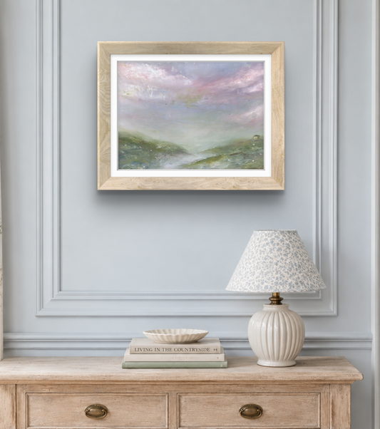Framed landscape painting on a wall above a wooden console table with a lamp and books.