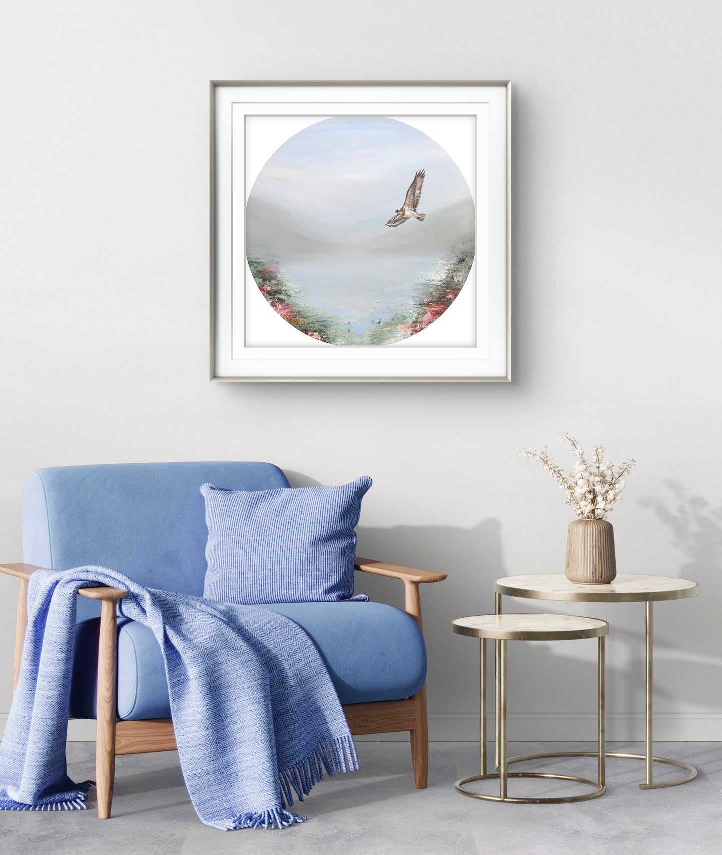 Framed artwork of a bird over water hanging above a blue armchair with a blanket and pillow.