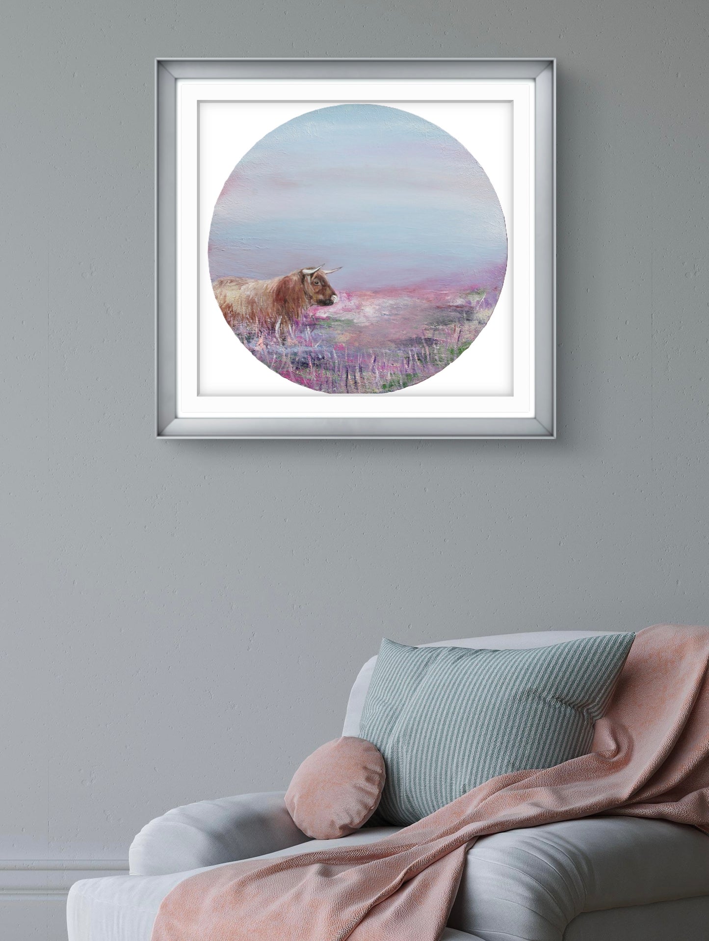 Framed artwork of a cow in a field on a grey wall above a sofa.