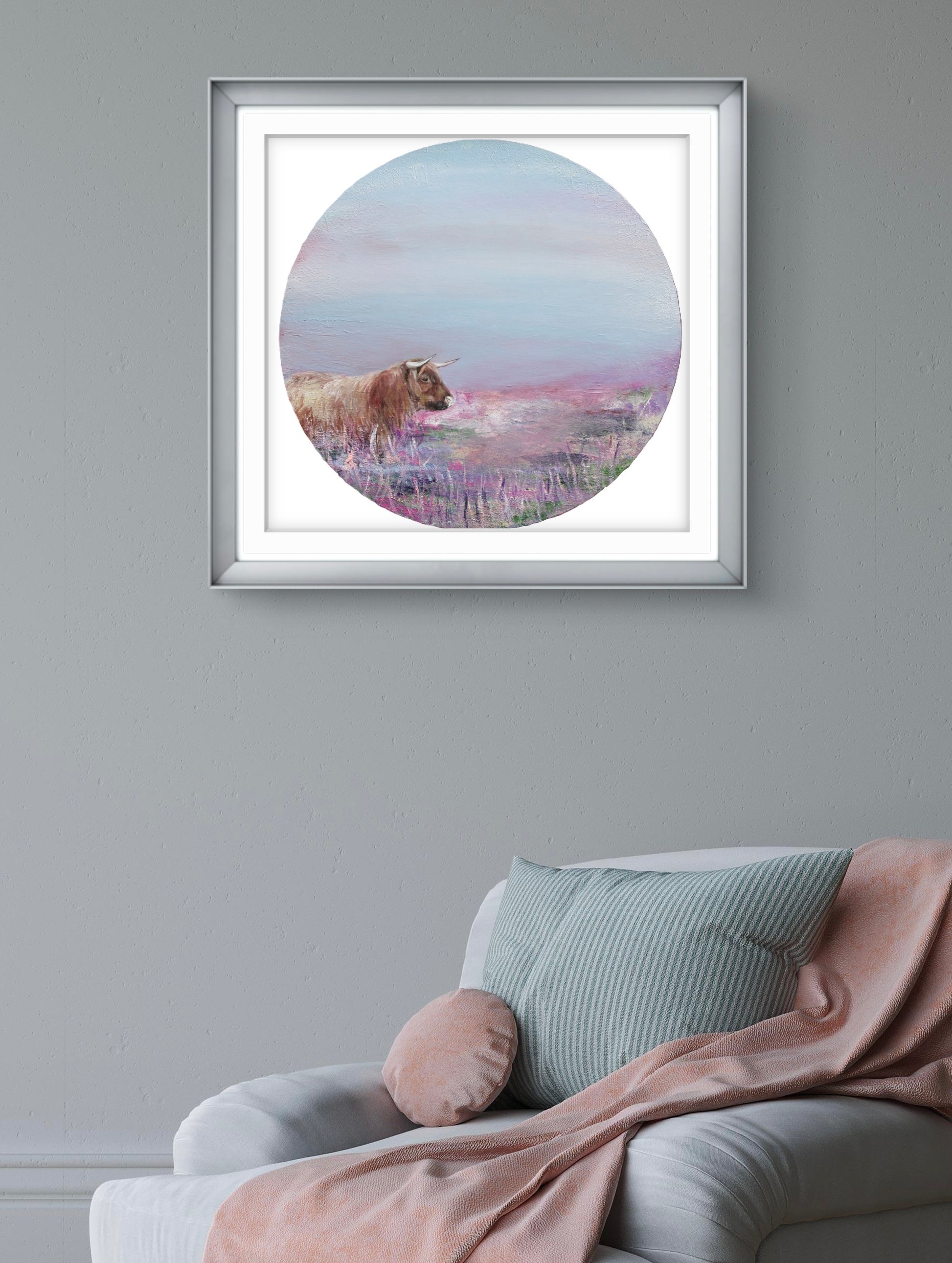 Framed artwork of a cow in a field on a grey wall above a sofa.