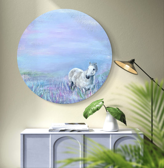 A round acrylic painting featuring a Highland pony in a field with a pastel-colored sky, mounted on a wall above a white console table with a green plant.