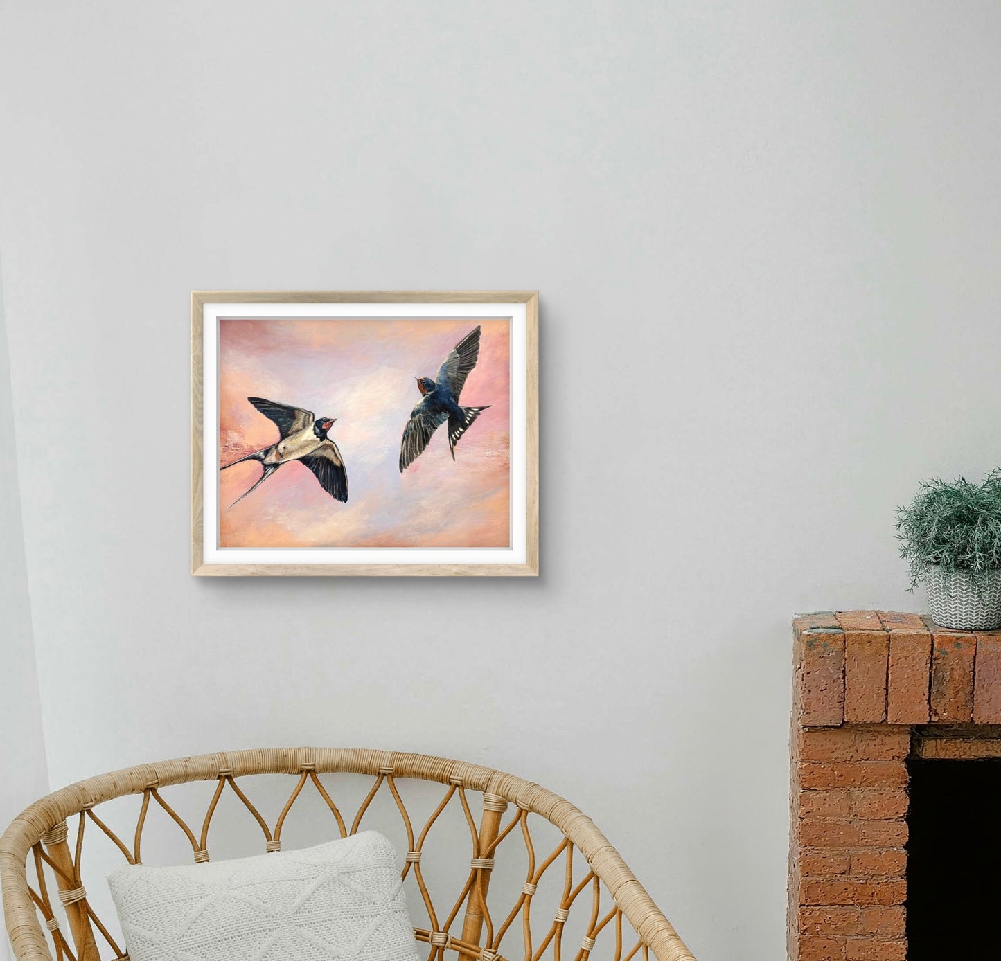 Framed artwork of two birds flying on a wall above a wicker chair.