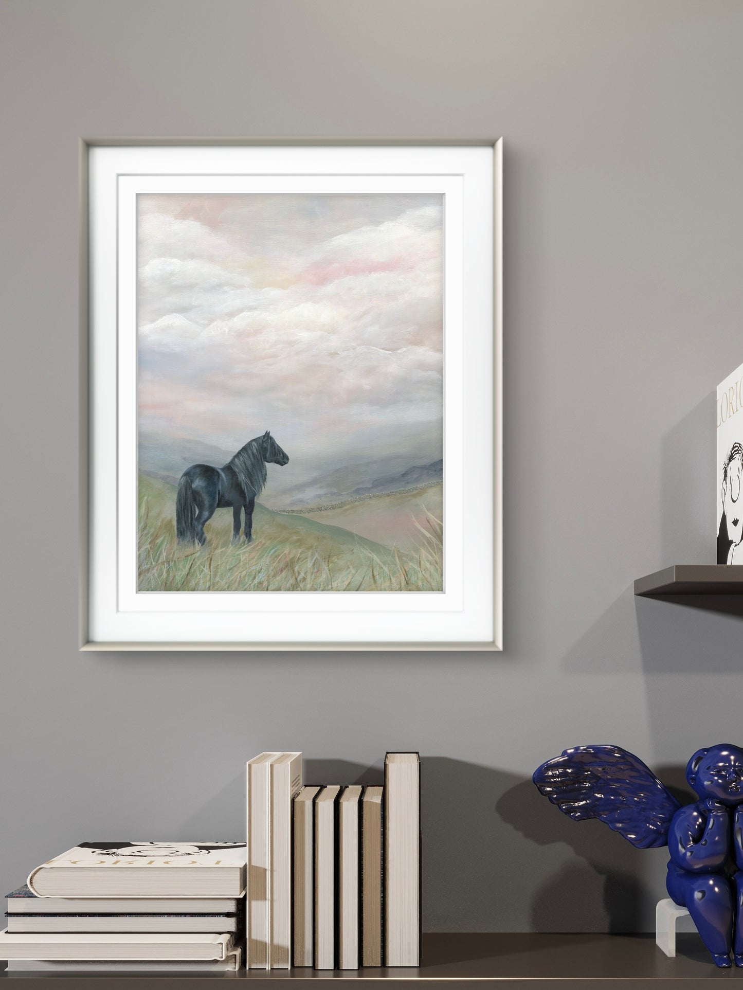 Black dales pony on a moorland art scene, framed in silver above a book shelf with books and ornaments on it 
