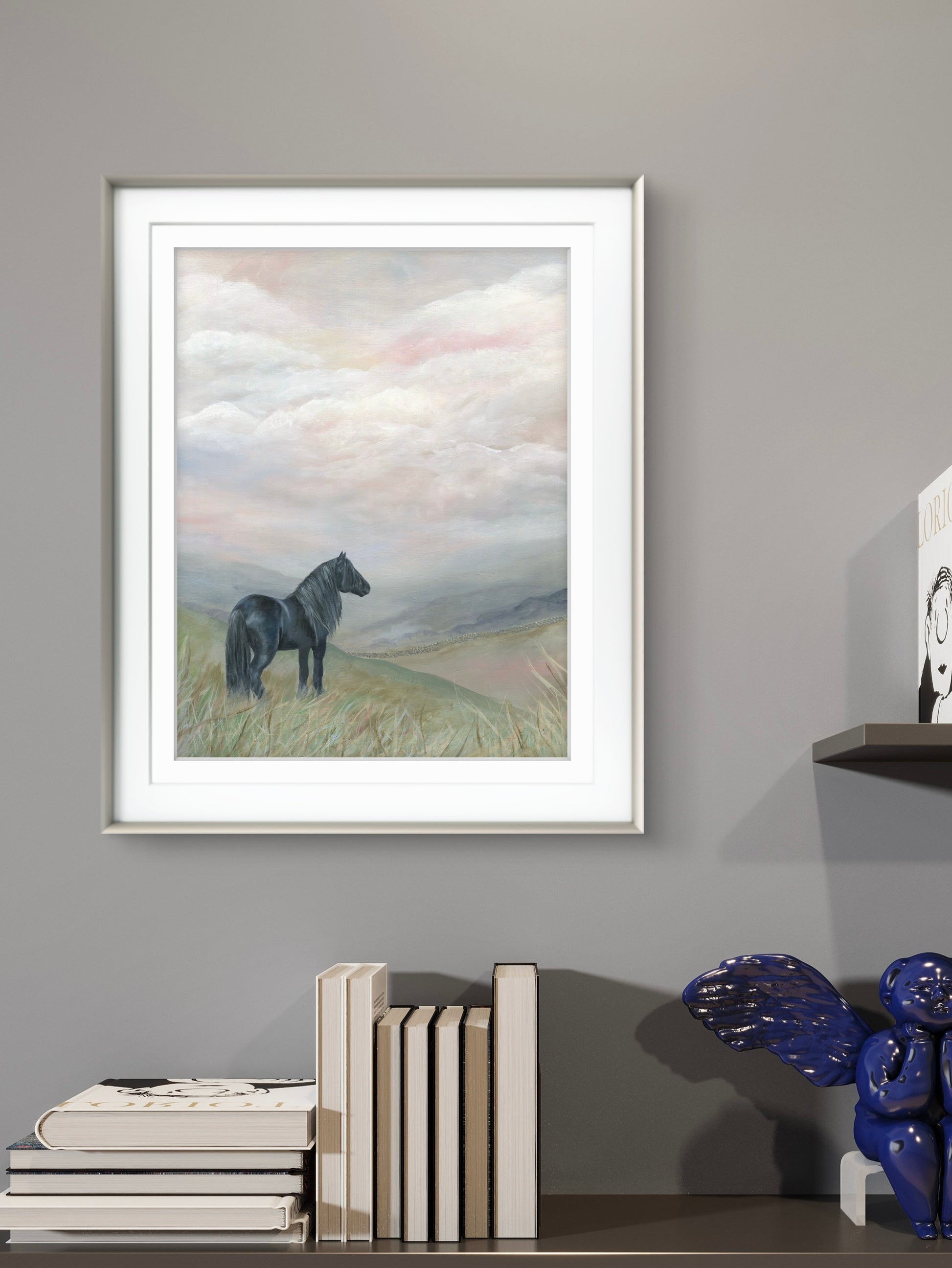 Black dales pony on a moorland art scene, framed in silver above a book shelf with books and ornaments on it 