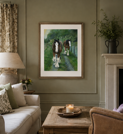 A framed painting of two draft horses walking along a path in a green field, displayed on a sage green wall in a styled living room setting.