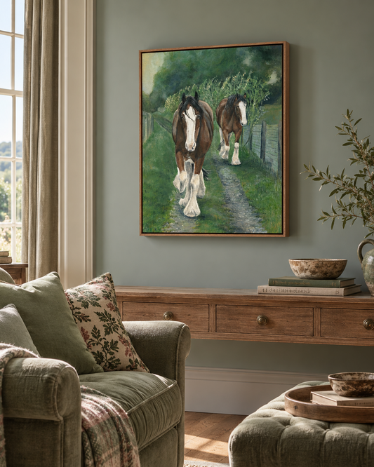 A framed painting of two brown and white horses walking along a dirt path in a green field, displayed on a sage green wall above a wooden console table in a styled living room.