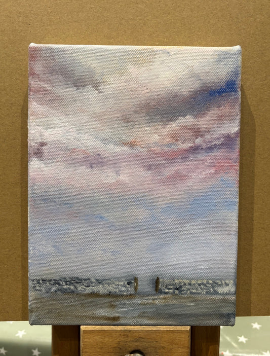 Small painting of a landscape with a cloudy sky against a brown background perched on an easel