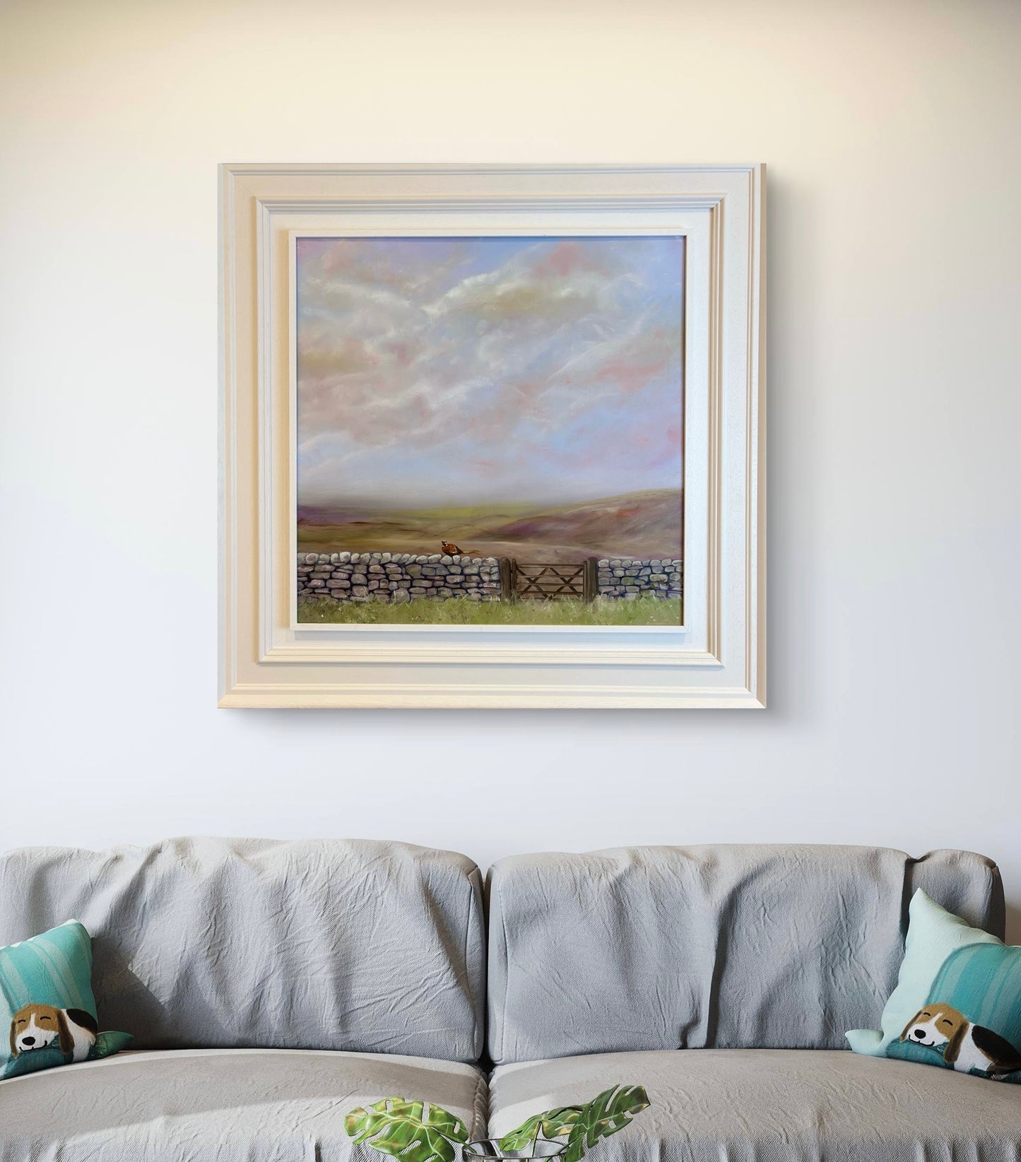 Framed landscape painting above a sofa with decorative pillows.