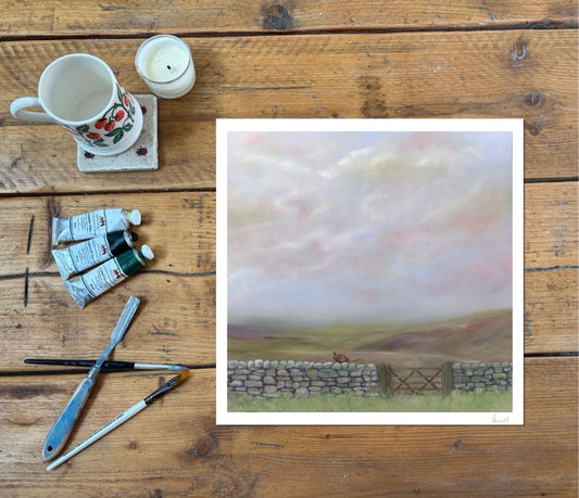 Countryside fine art print depicting moorland scenes and drystone wall with a pheasant, on a wooden rustic table with paint and brushes by the side
