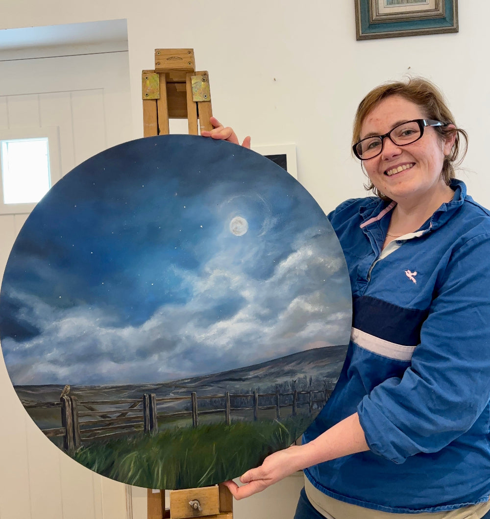 Person holding a painting of a landscape with a night sky.