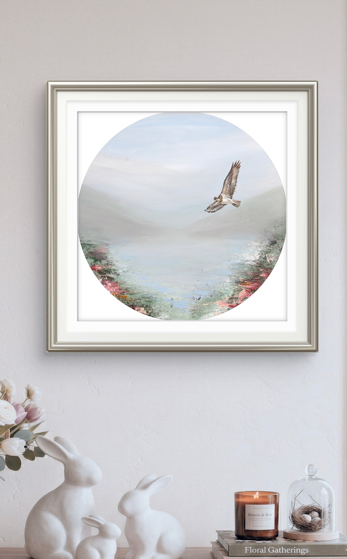 Framed artwork of a bird flying over a landscape on a wall with decorative items below.
