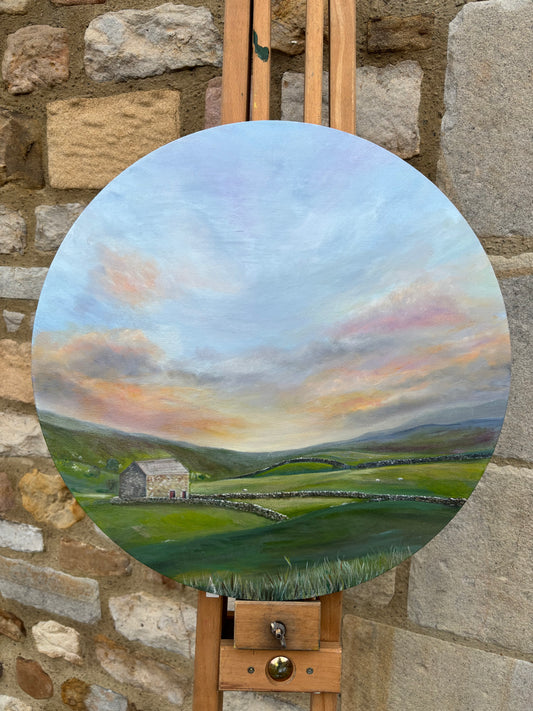 Round landscape painting on an easel against a stone wall