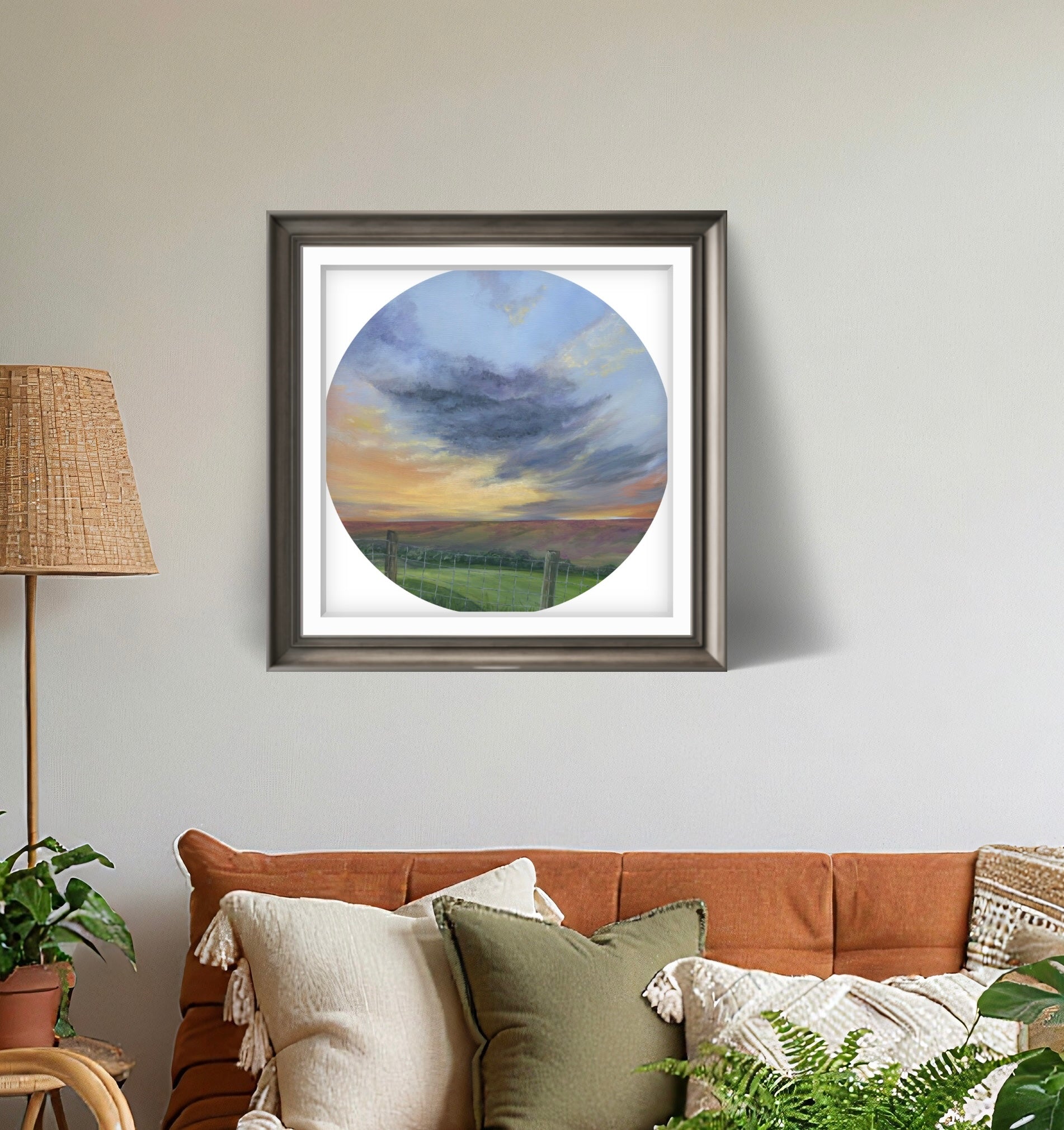 Framed artwork of a sunset over a field on a wall above a sofa.