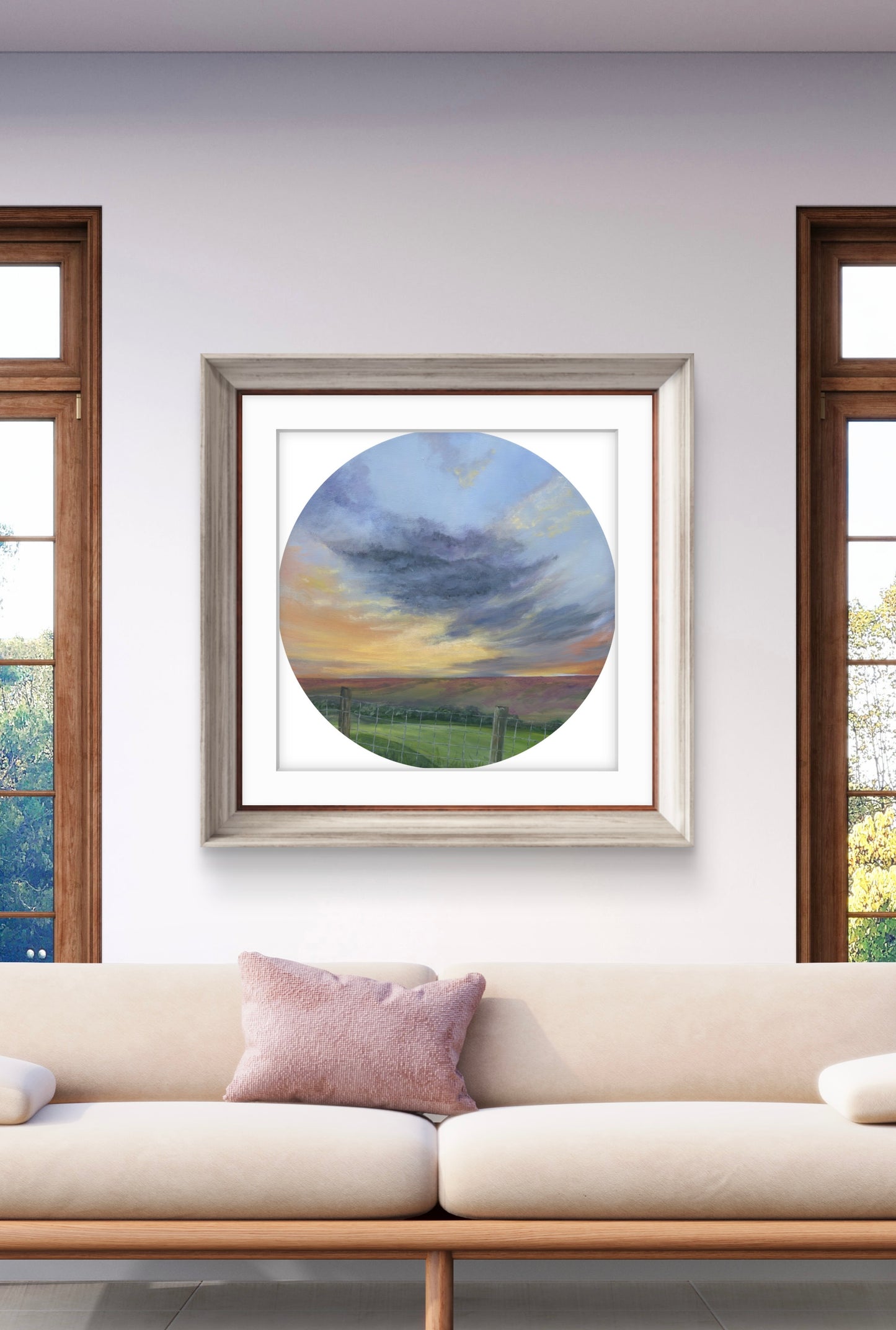 Framed artwork of a circular landscape scene on a wall above a sofa.