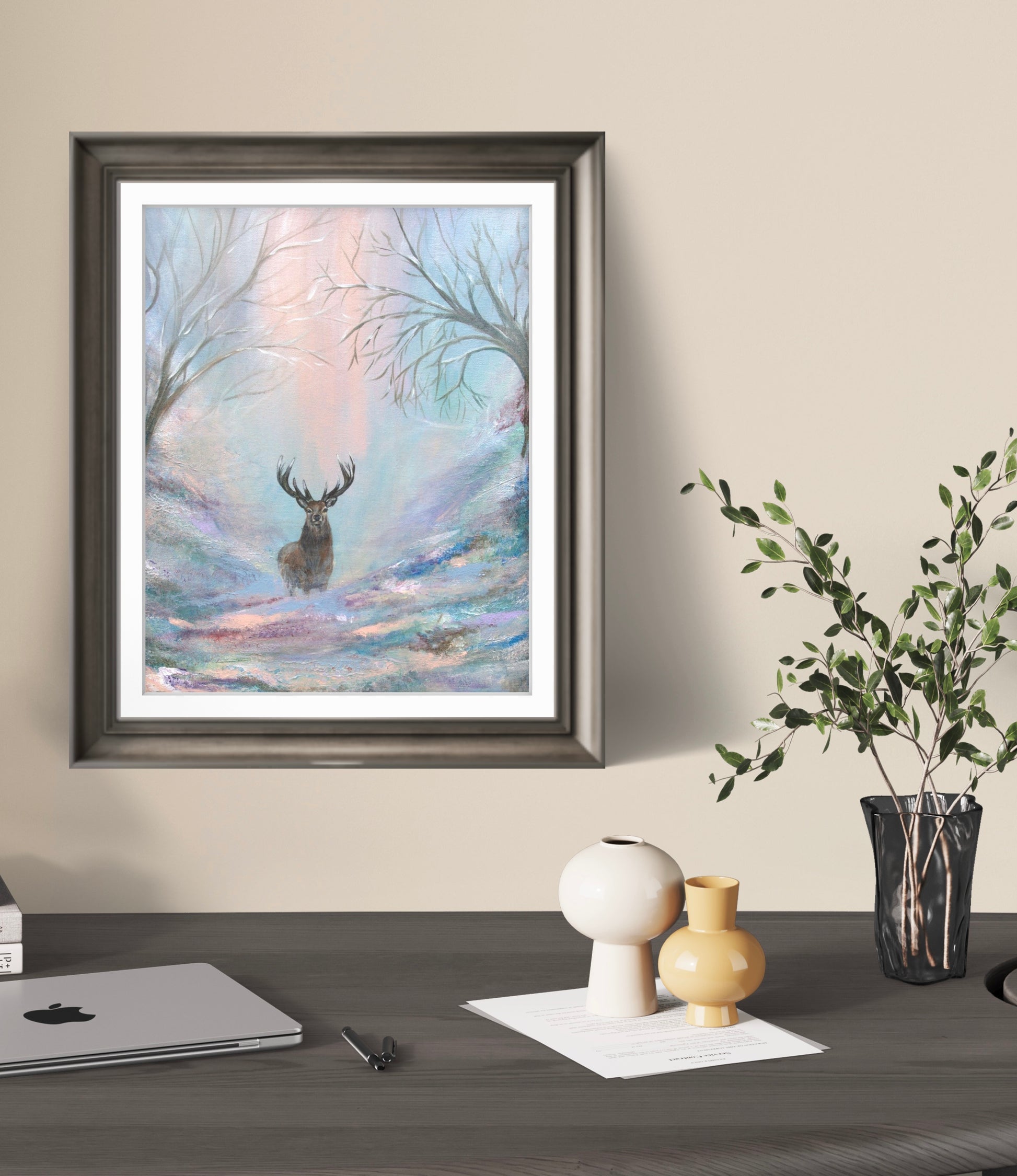 Framed artwork of a deer in a forest scene on a wall above a desk.